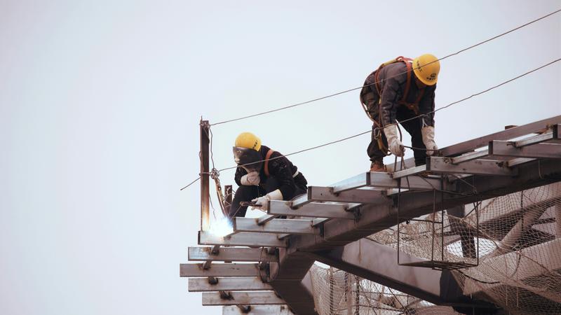A man wearing a black jacket and yellow hard hat at a construction site
